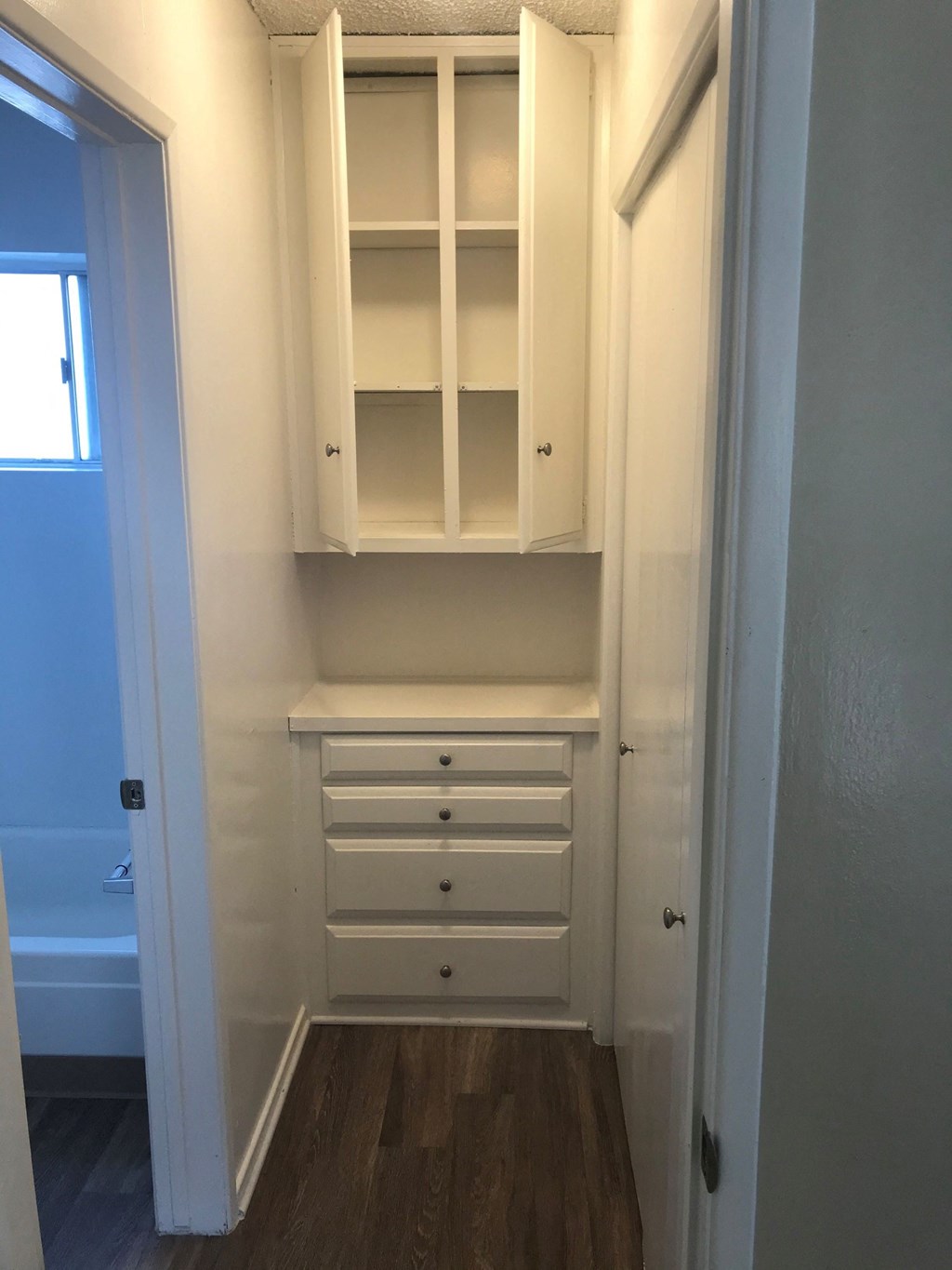 a closet in a bathroom with white cabinets and drawers