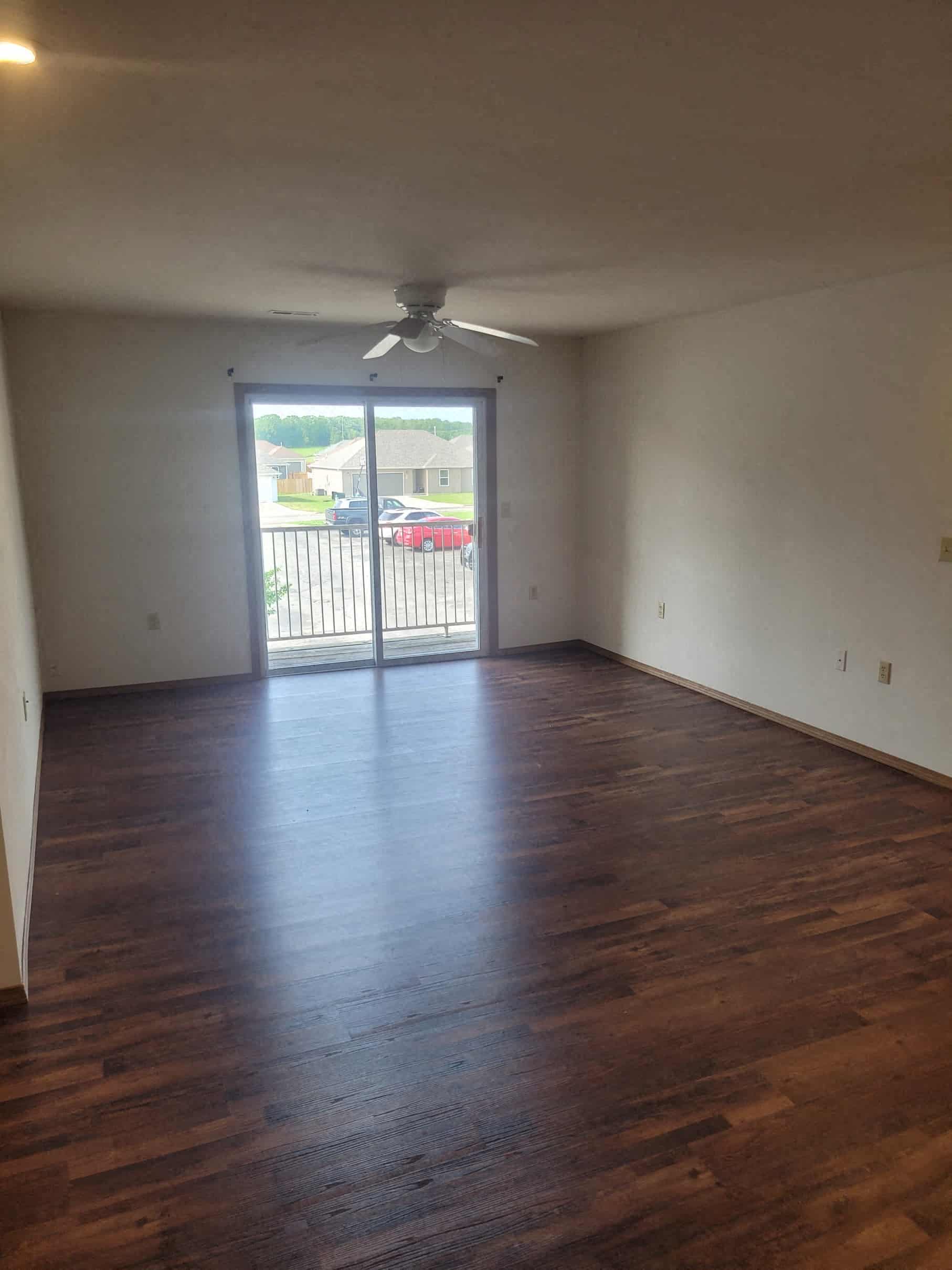 an empty living room with hard wood floors and a sliding glass door