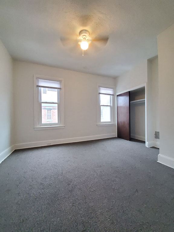 an empty living room with a ceiling fan and two windows