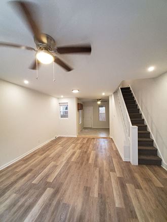 an empty living room with a ceiling fan and stairs