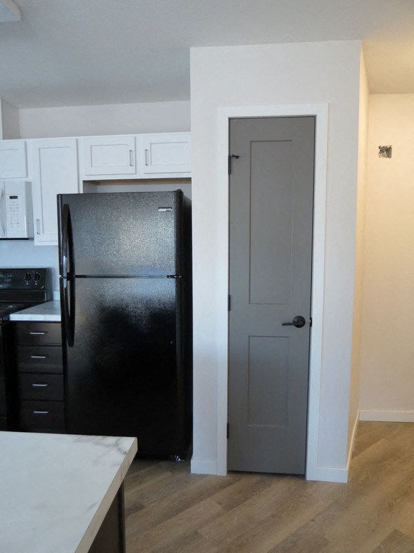 a kitchen with black refrigerator and white cabinets and a door