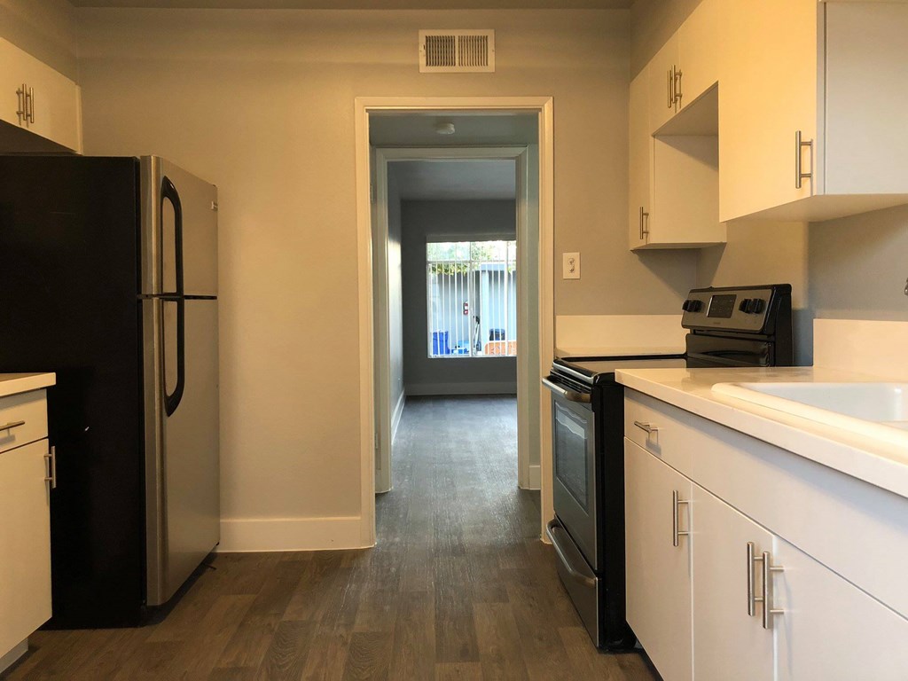 a kitchen with white cabinets and black appliances and a hallway with a door to a