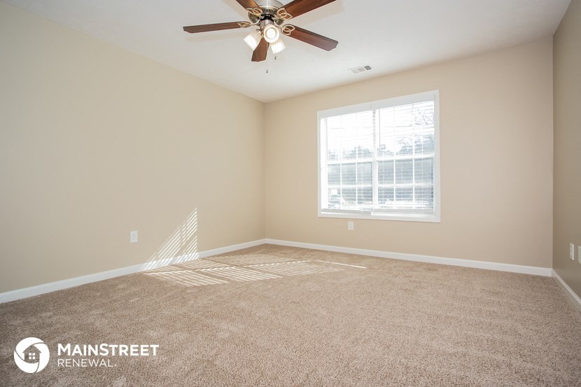 the spacious living room with carpeted flooring and a ceiling fan