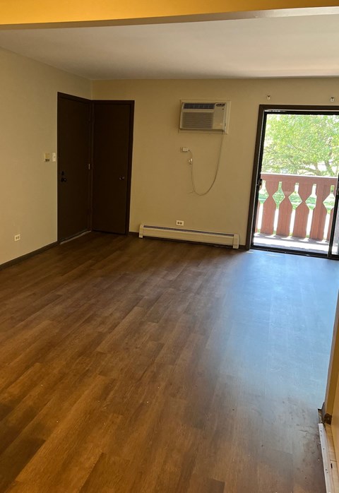 A room with wooden floors and a balcony with a view of trees.