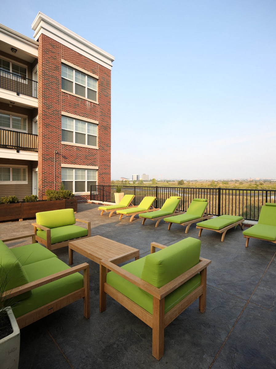 a rendering of a patio with green lounge chairs and a brick building