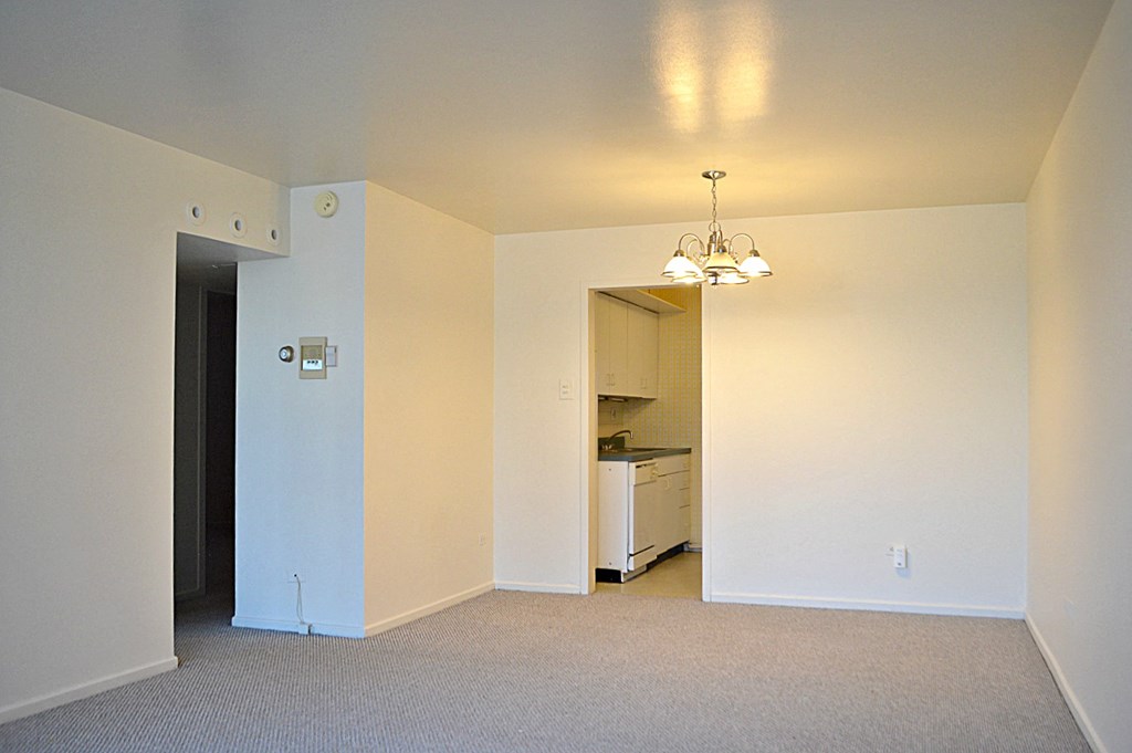 an empty living room with a kitchen in the background