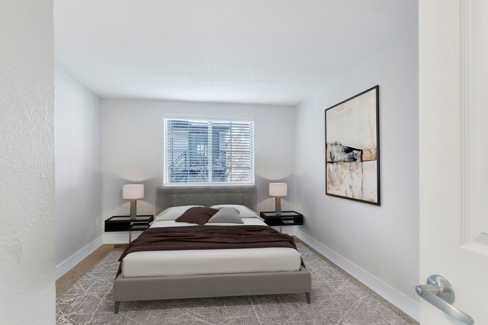 A bedroom with a large bed and a window with blinds.
