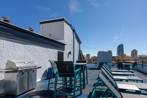 the rooftop deck of the building has tables and chairs and a grill