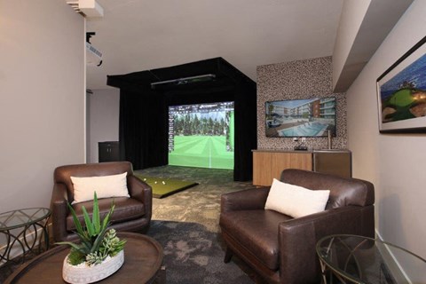 a living room with two leather chairs and a view of a golf simulator