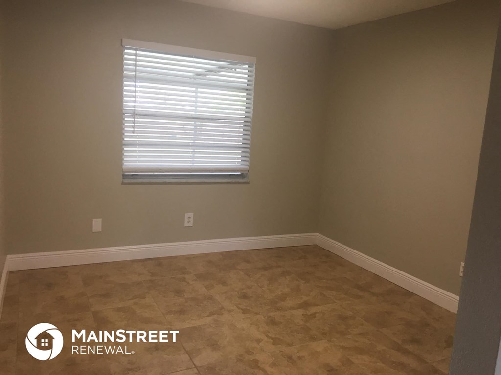 an empty room with a window and brown flooring