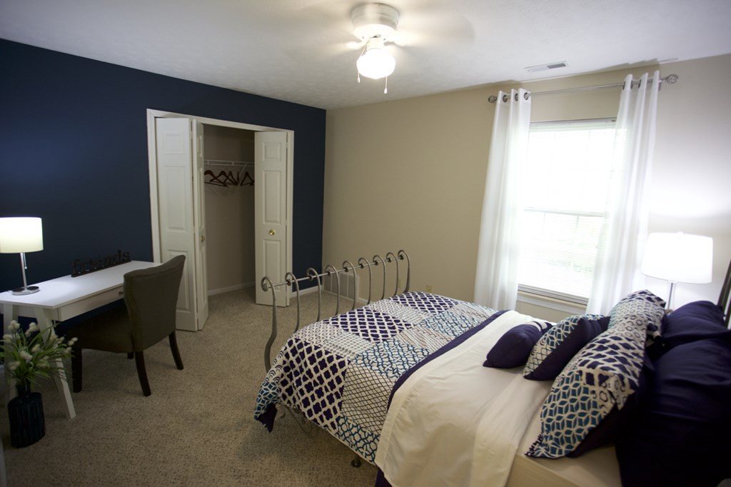 a bedroom with a bed and a desk and two windows