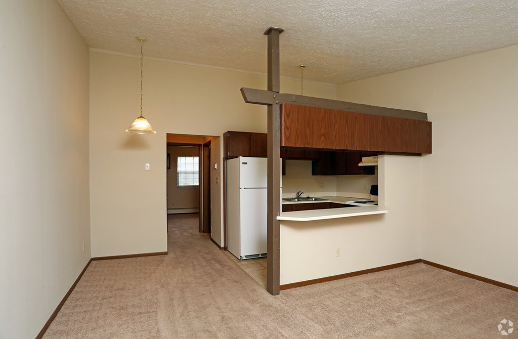 an empty living room with a kitchen and a refrigerator
