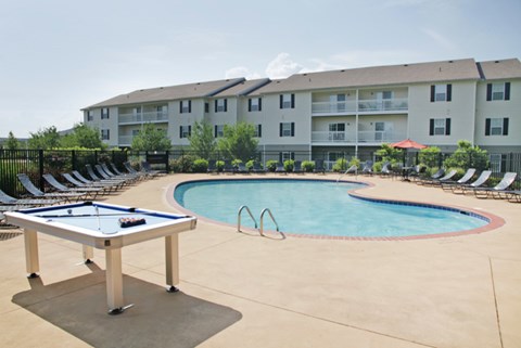 an outdoor pool with a shuffleboard table and an apartment building
