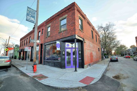 A red brick building with a purple door and a sign that says West Plaza.