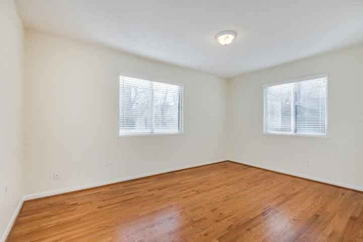 an empty room with wooden floors and two windows