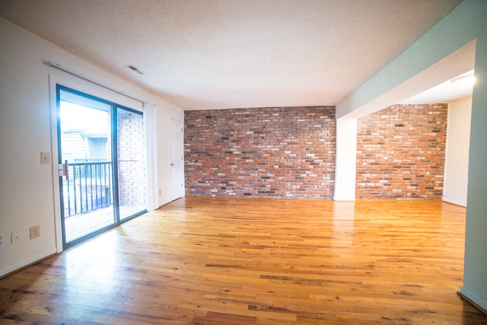 an empty living room with wood floors and a brick wall