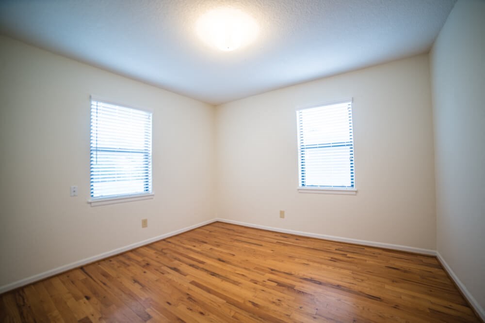an empty room with wooden floors and two windows