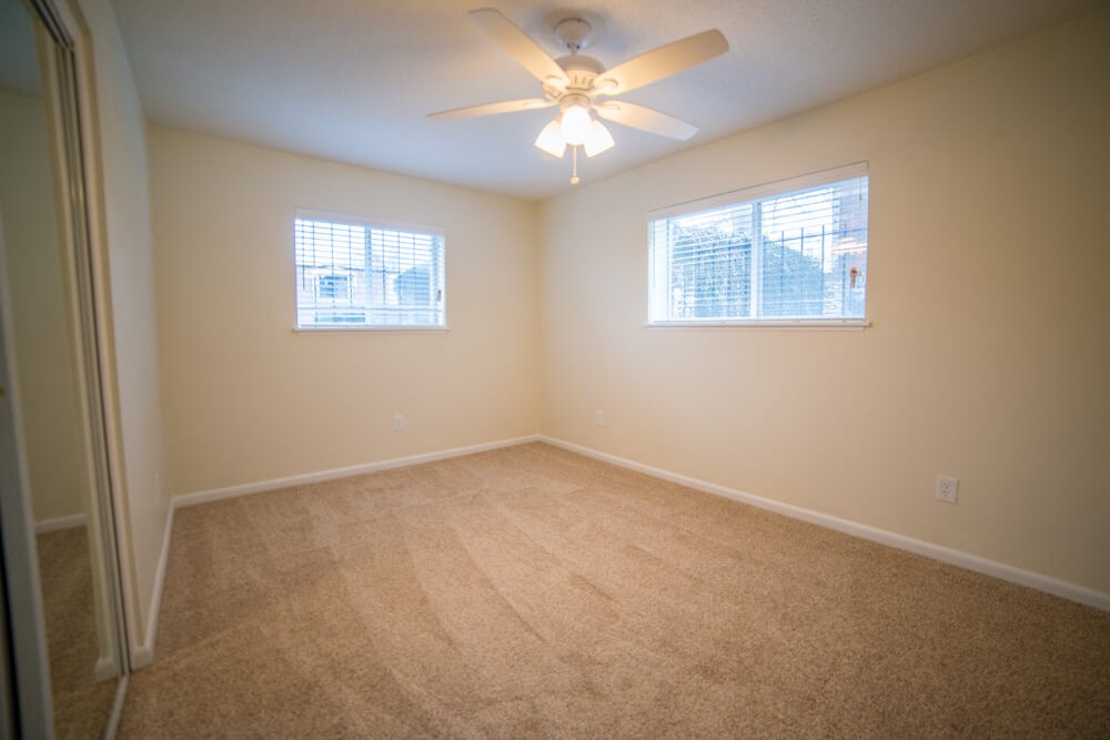 a empty room with a ceiling fan and two windows
