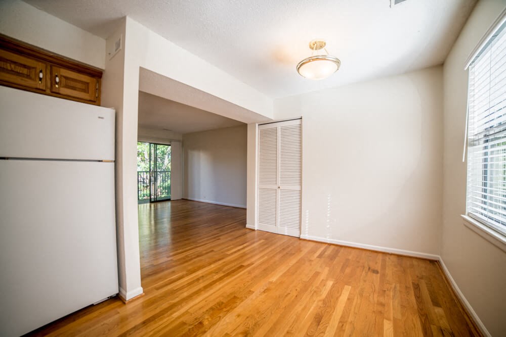 an empty living room and kitchen with a refrigerator and wood floors