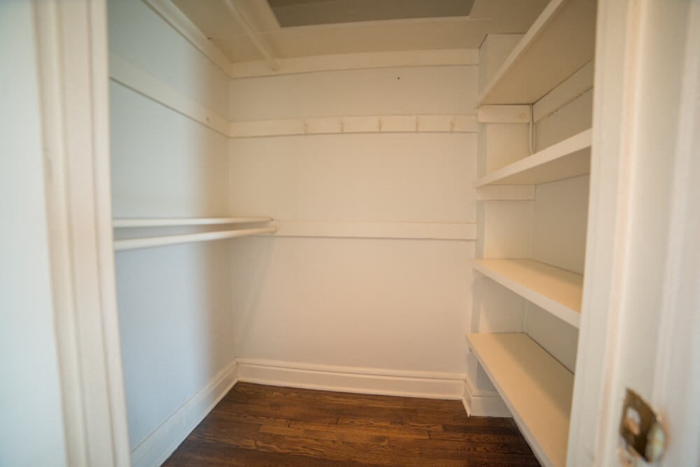 a walk in closet with white shelves and a wood floor
