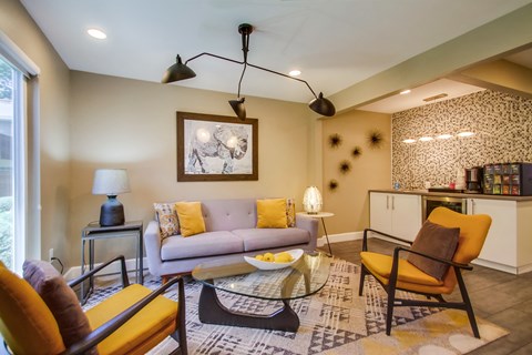 A living room with a grey couch, yellow chairs, and a glass coffee table.