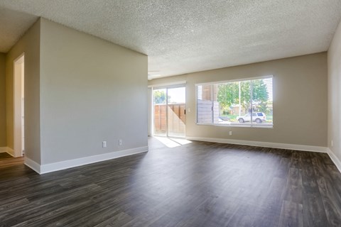 A spacious room with wooden flooring and a view of a street through the window.