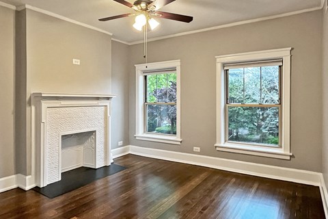 A room with a fireplace, two windows, and a ceiling fan.