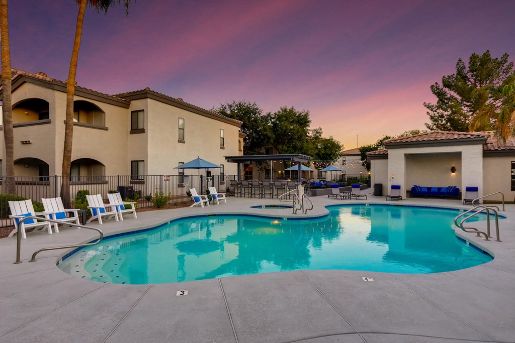 a resort style swimming pool with chairs around it at dusk