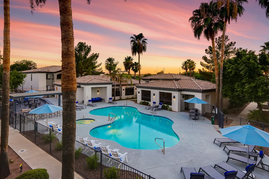 a swimming pool with chairs and umbrellas at sunset