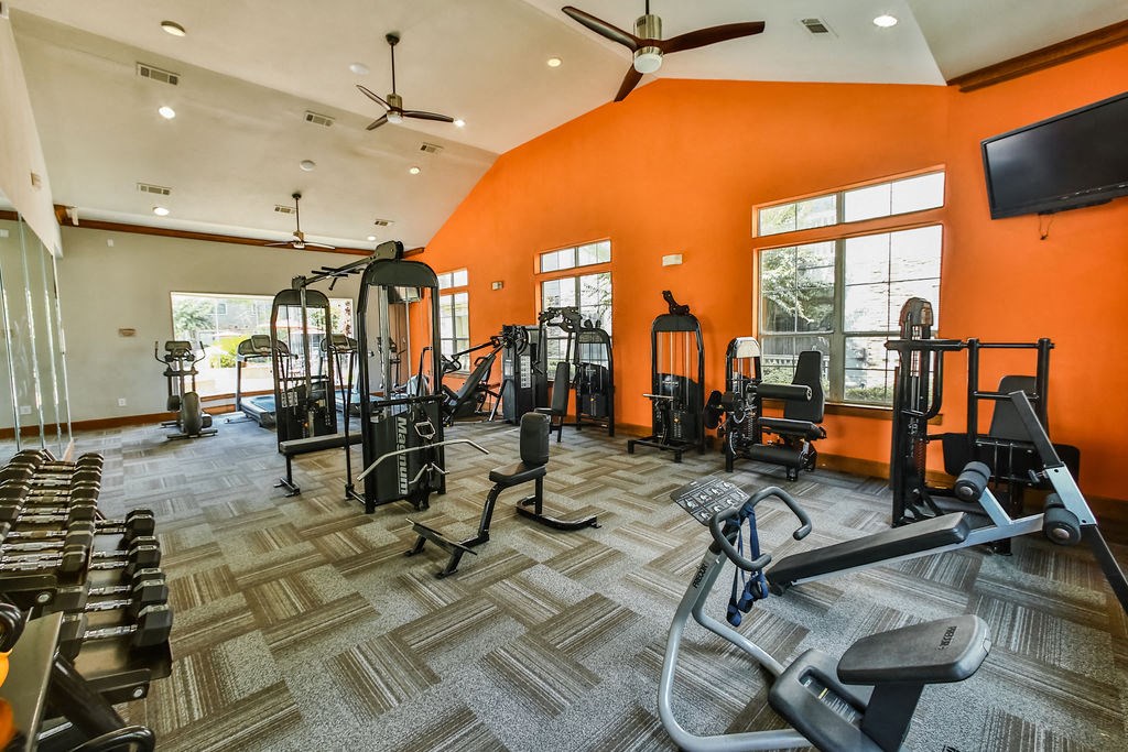 a gym with weights and cardio equipment in a home with an orange wall and windows