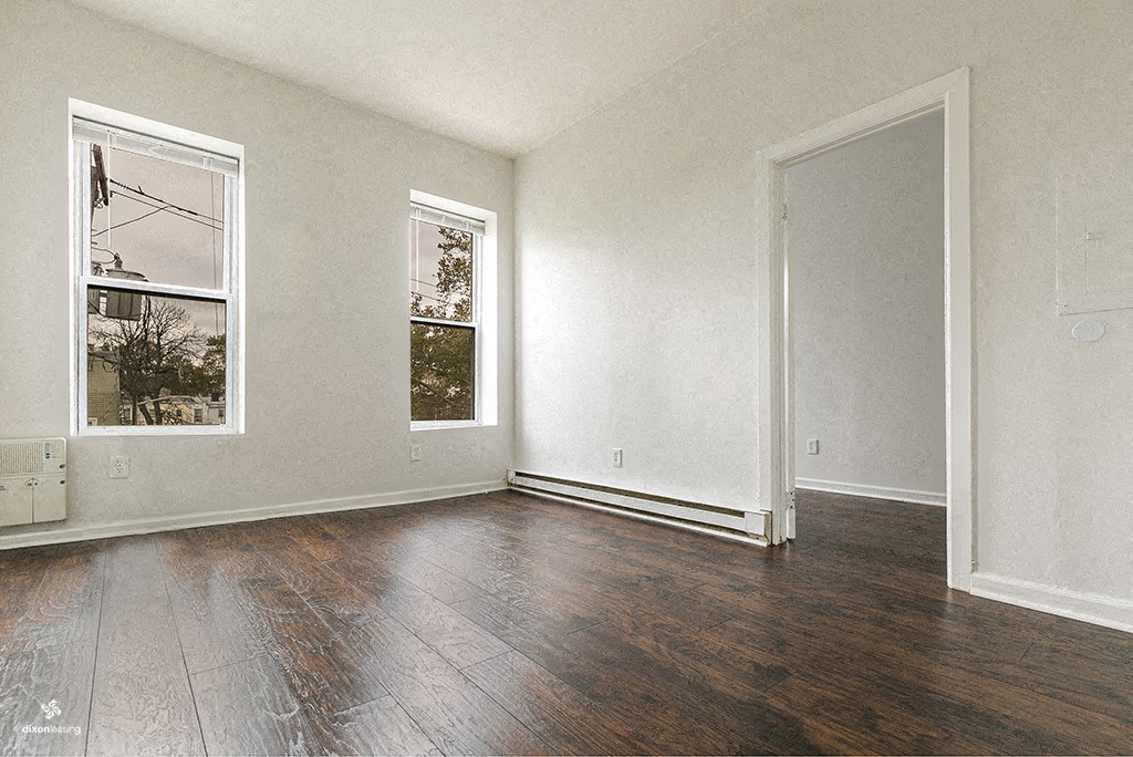 an empty living room with hard wood floors and two windows