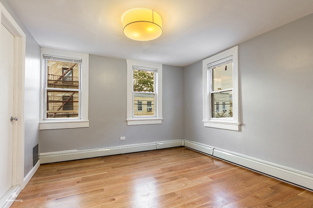 an empty room with wooden floors and three windows
