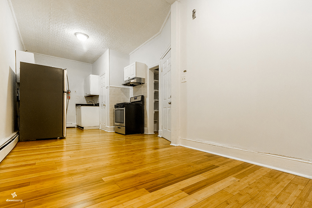 an empty living room with a wood floor and a refrigerator
