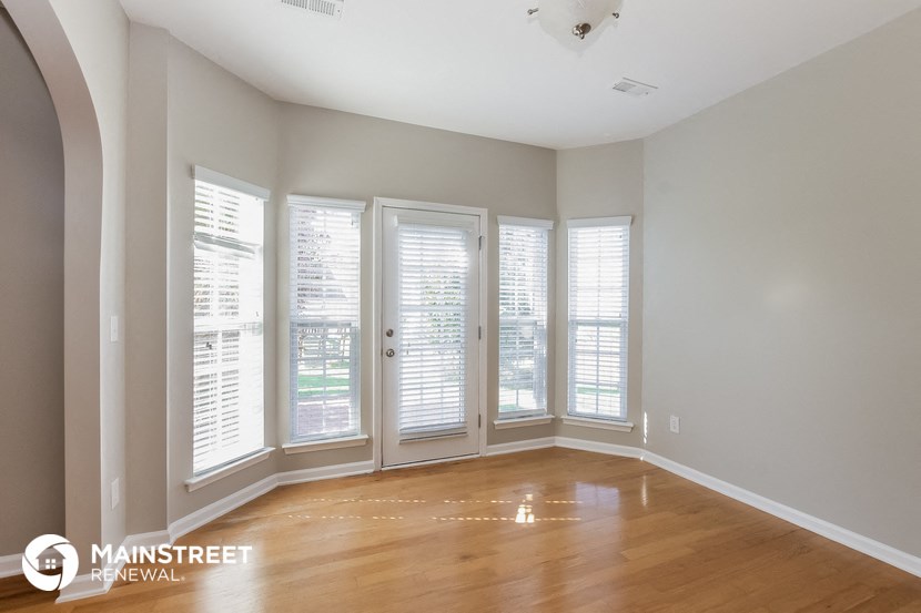 a living room with windows and a wood floor and a door to a balcony