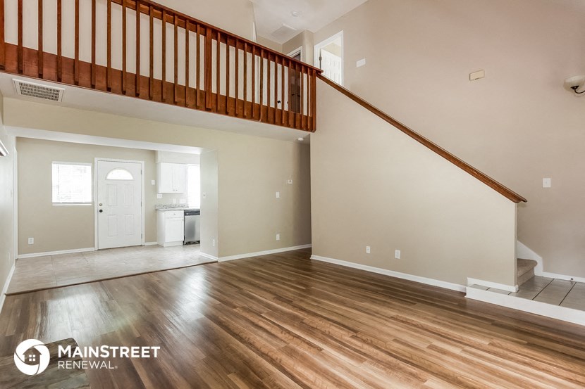 the living room and entryway of a home with wood flooring and a staircase