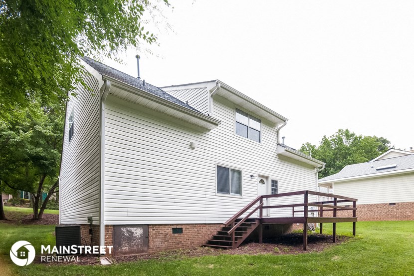 the back of a white house with a deck and a tree