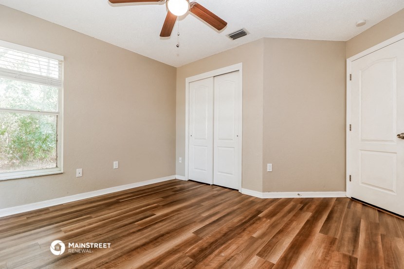 the spacious living room with hardwood flooring and a ceiling fan