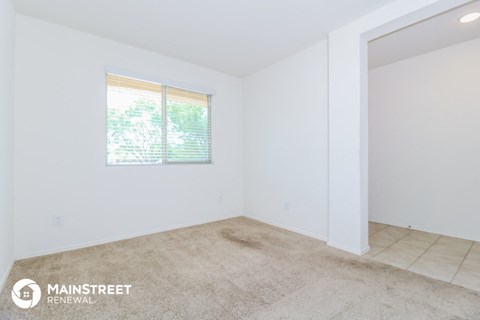 the living room of a small white house with carpet and a window