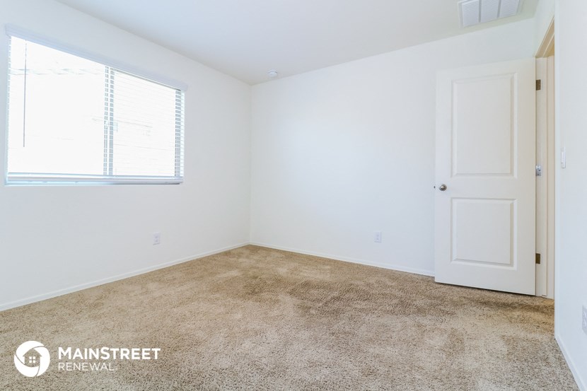 the bedroom of a small white house with carpet and a window