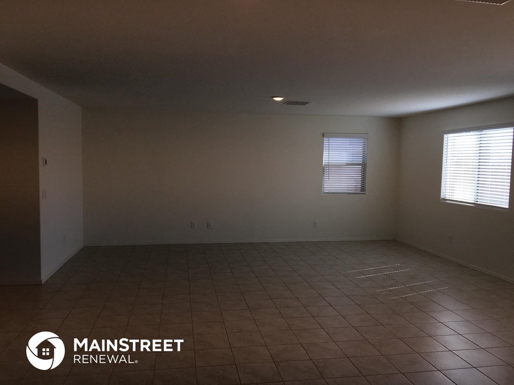 an empty living room with a tiled floor and two windows