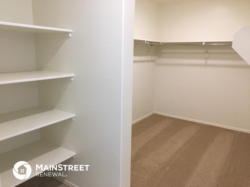 a walk in closet with white shelves and a wood floor