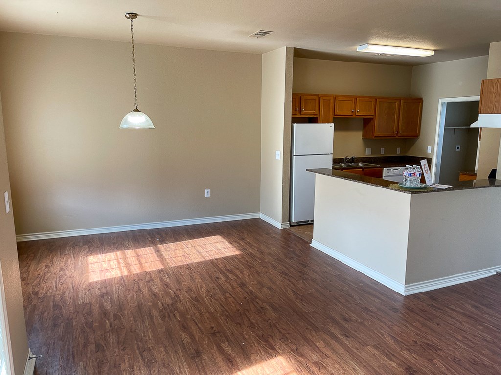 an empty living room with wood floors and a kitchen