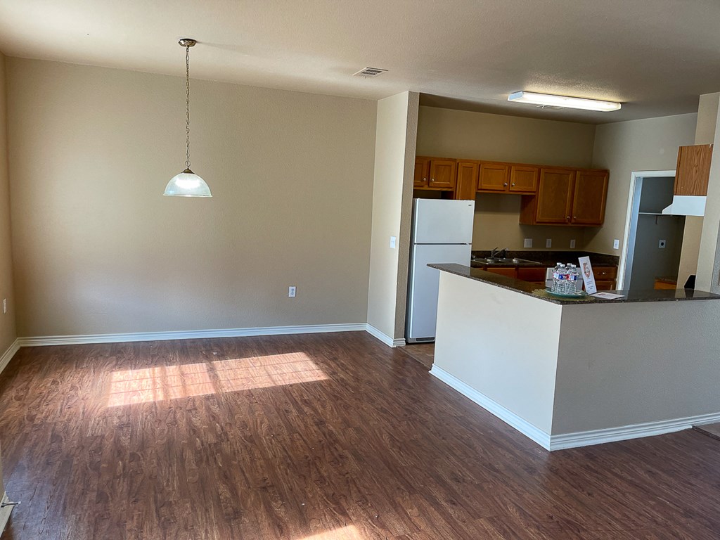 an empty living room with wood floors and a kitchen