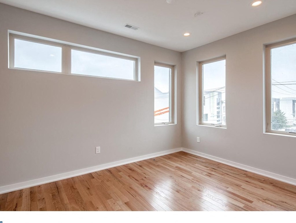 an empty living room with wood floors and three windows