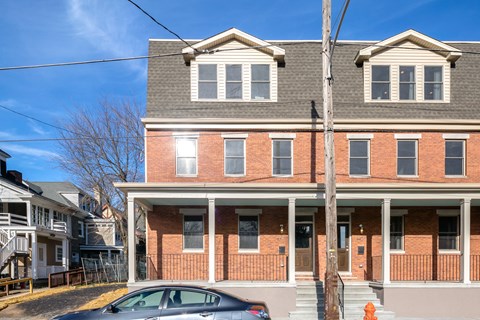 A two-story brick house with a car parked in front.