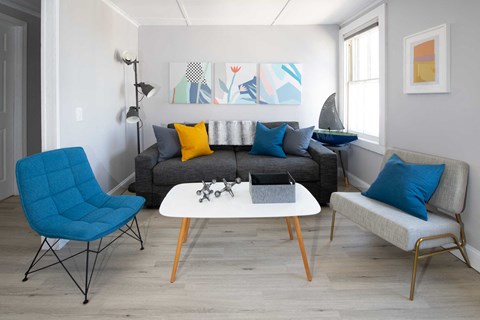 a living room with a gray couch and a white table and blue chairs