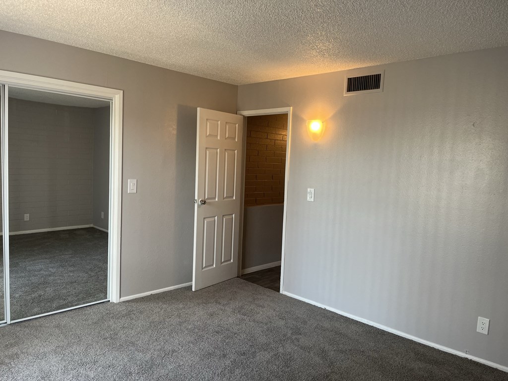 an empty living room with a white door and a hallway to a bedroom