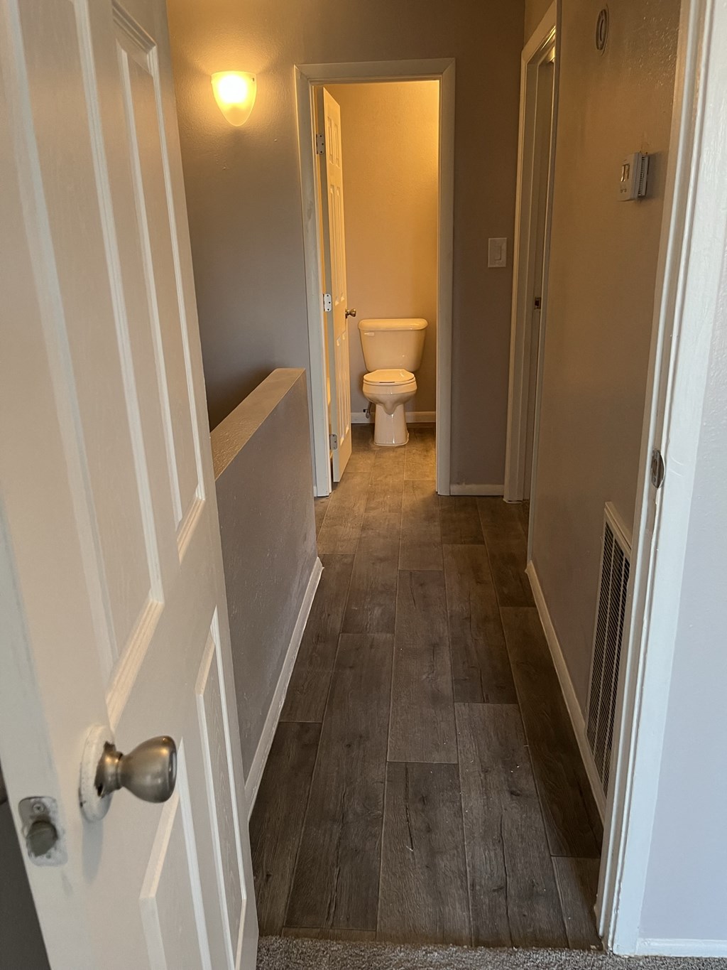 a hallway with a door and a bathroom with a toilet