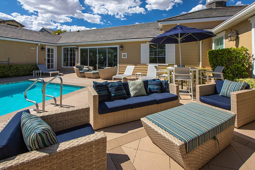 a pool and patio with chairs and umbrellas in front of a house