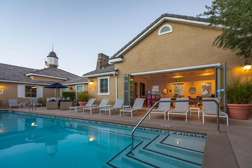 a swimming pool in front of a house with a pool table and chairs